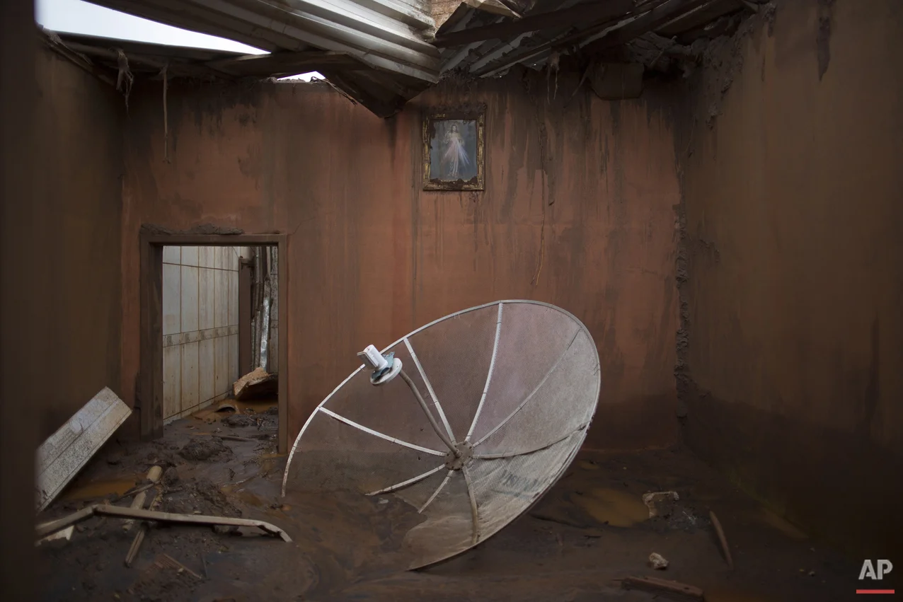 In this Nov. 23, 2015 photo, a satellite dish sits amid debris in a home destroyed when dams of an iron ore mine burst in early November, causing a mudslide, in the village of Bento Rodrigues, Brazil. The village, in the central state of Minas Gerais, was home to about 600 people until Nov. 5, when the dam burst, unleashing a tsunami of mud that swept away nearly everything in its path, flattening houses, uprooting trees and tossing cars asunder. (AP Photo/Leo Correa)