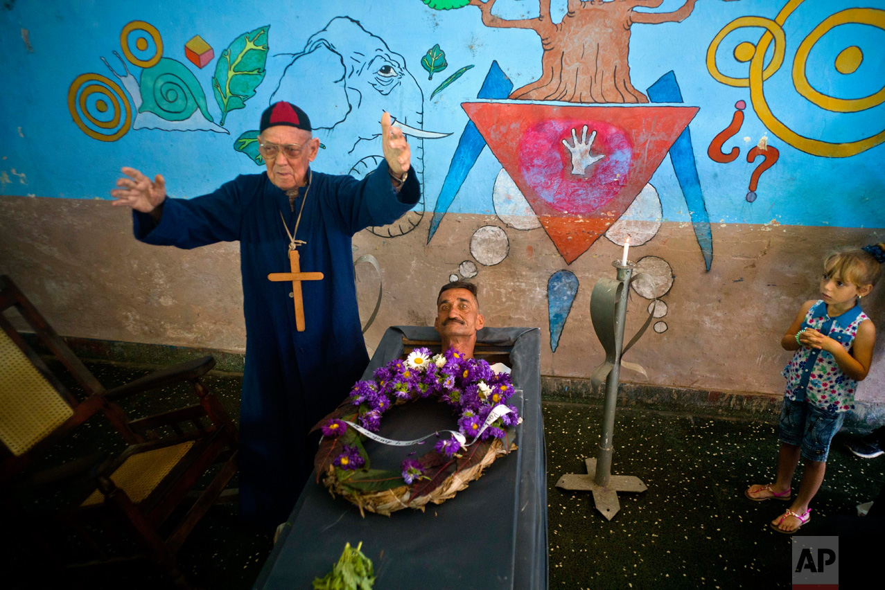 Marcelino Rogelio Estrada performs the role of a priest during the annual celebration known as the Burial of Pachencho, played by Divaldo Aguiar, who lies in a coffin during the mock funeral service, in Santiago de Las Vegas, Cuba, Sunday, Feb. 5, 2017. Residents stage the mock funeral and burial of Pachencho in a boozy festival that has become an annual tradition to mark the end of the local carnival season. (AP Photo/Ramon Espinosa)