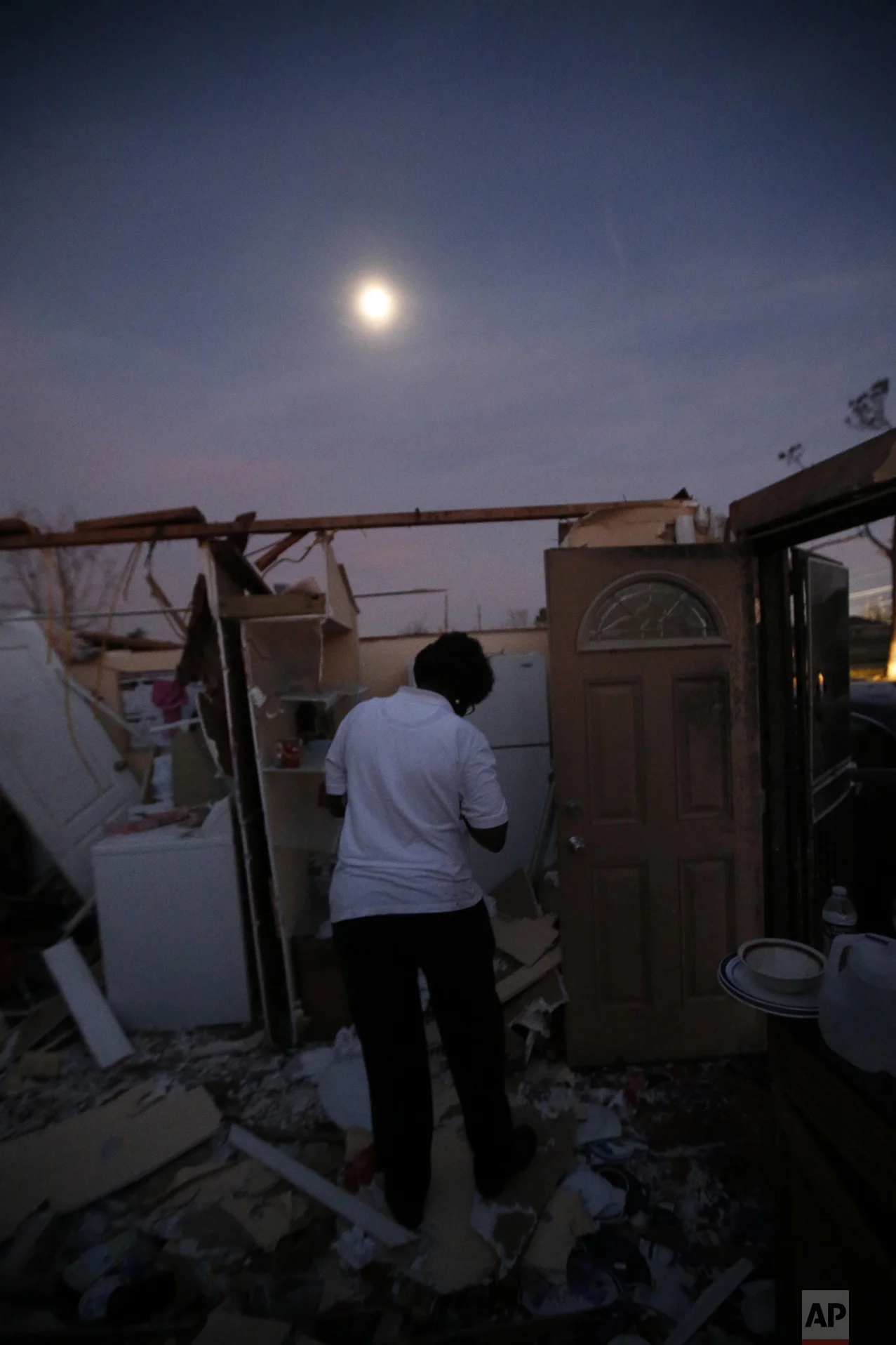 With a moon rising overhead, Theresa Perkins retrieves some belongings from inside of the destroyed home of her friend, Thelma Packnett, in the aftermath of Tuesday's tornado that tore through the New Orleans East section of New Orleans, Wednesday, Feb. 8, 2017. (AP Photo/Gerald Herbert)