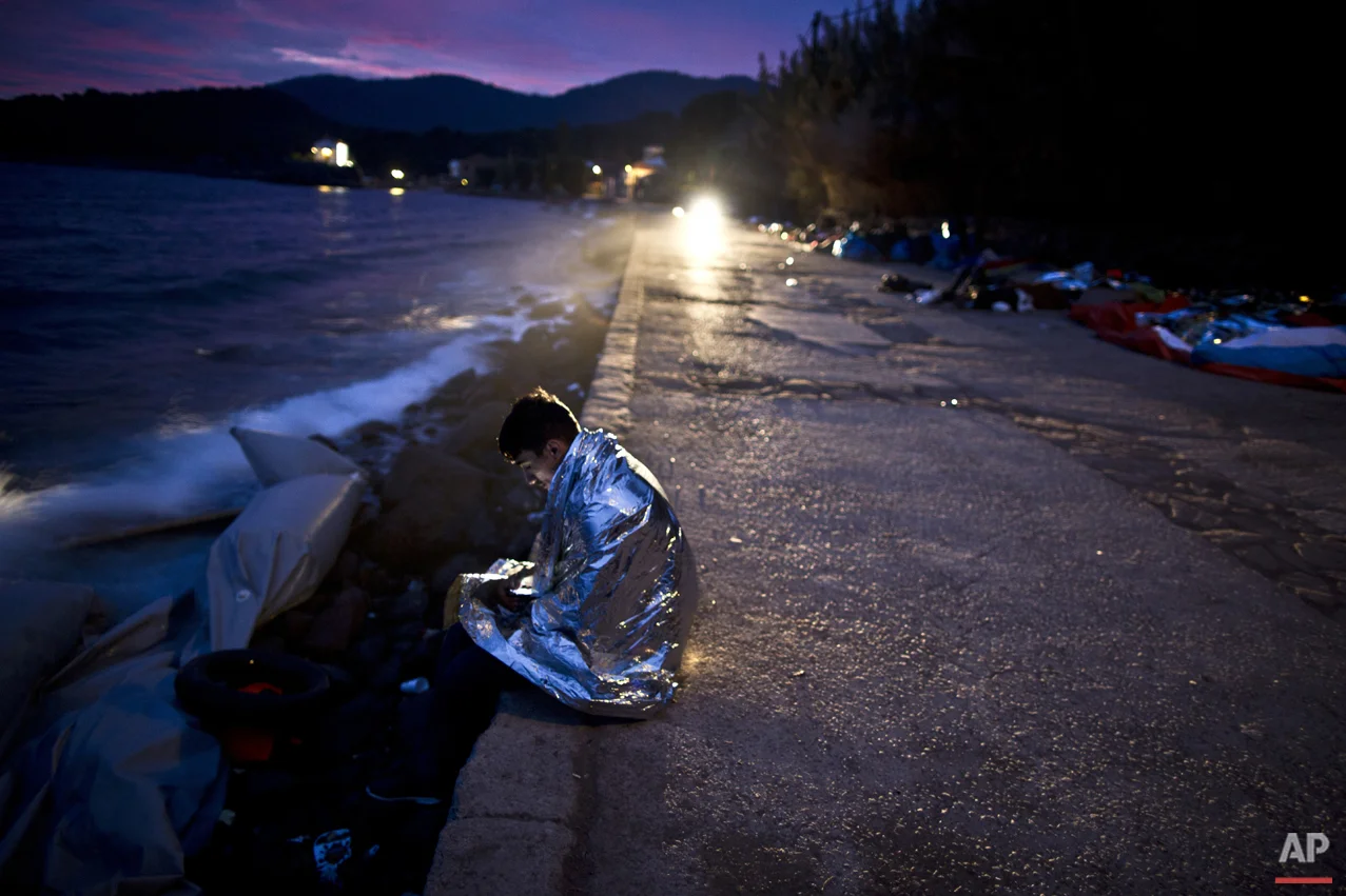 An Afghan refugee wrapped, in a thermal blanket faces the sea after he and others arrived late in the night on a dinghy from the Turkish coast to the northeastern Greek island of Lesbos, early Thursday, Oct. 8 , 2015. (AP Photo/Muhammed Muheisen)