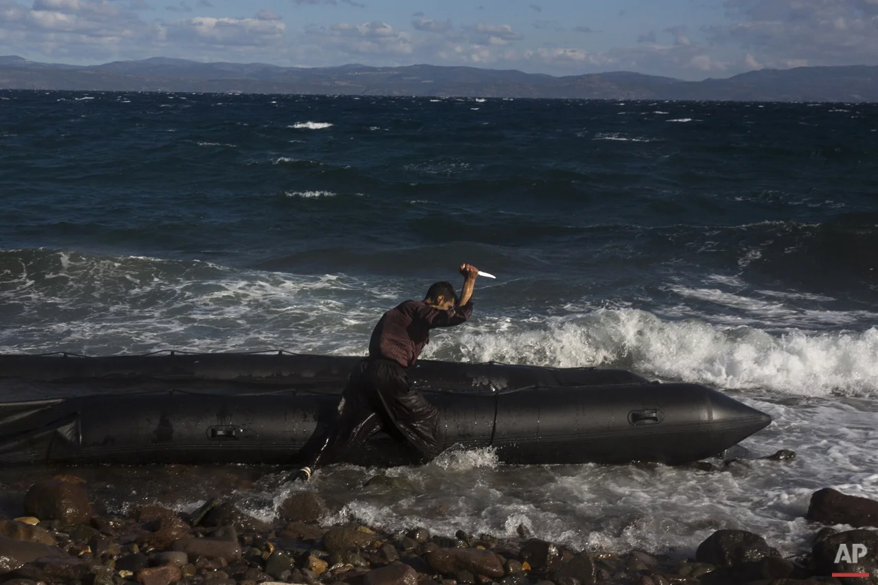 Afghan migrant uses a knife to puncture the dinghy in which he crossed with others from Turkey to the Greek island of Lesbos, Wednesday, Oct. 28, 2015. (AP Photo/Santi Palacios)