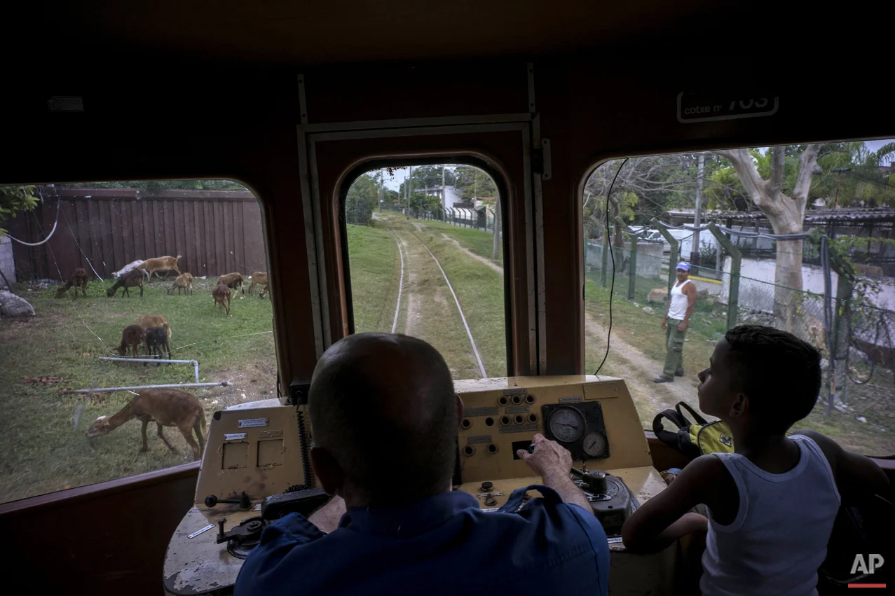 In this Aug. 26, 2015 photo, a boy rides next to the engineer of an electric Hershey train in the Casablanca municipality of Havana, Cuba. The conductor slowed the train down to avoid hitting a shepherd's flock of goats grazing along the tracks. (AP Photo/Ramon Espinosa)
