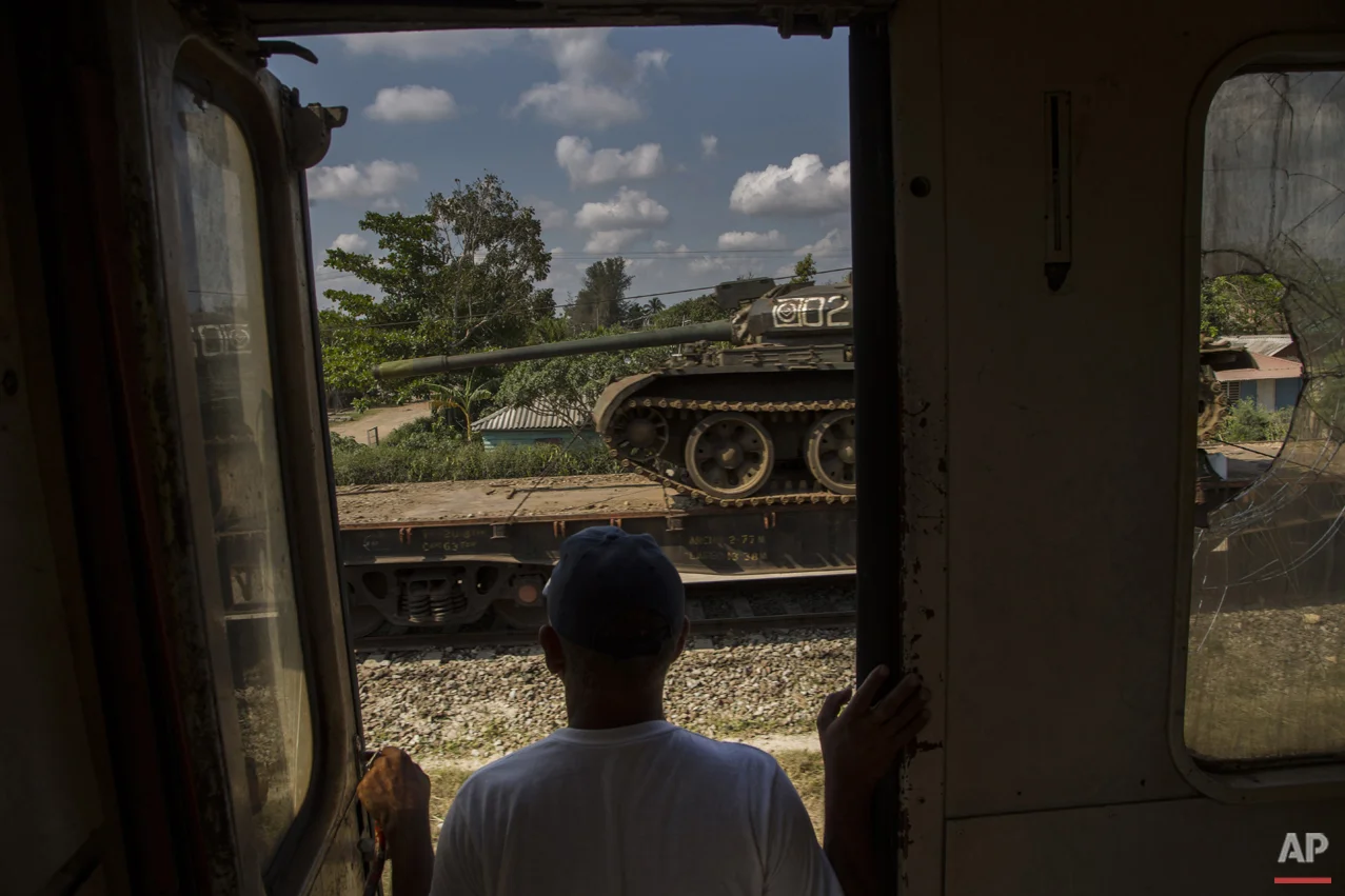 In this March 23, 2015 photo, a man looks at a tank being transported on a paused cargo train, as he travels by train through the province of Holguin, Cuba. The train system suffered along with much of the country’s infrastructure when the Soviet Union’s collapse cut Cuba off from the subsidies that Moscow had pumped into its economy. Currently, a longstanding U.S. trade embargo makes it hard to get parts. (AP Photo/Ramon Espinosa)