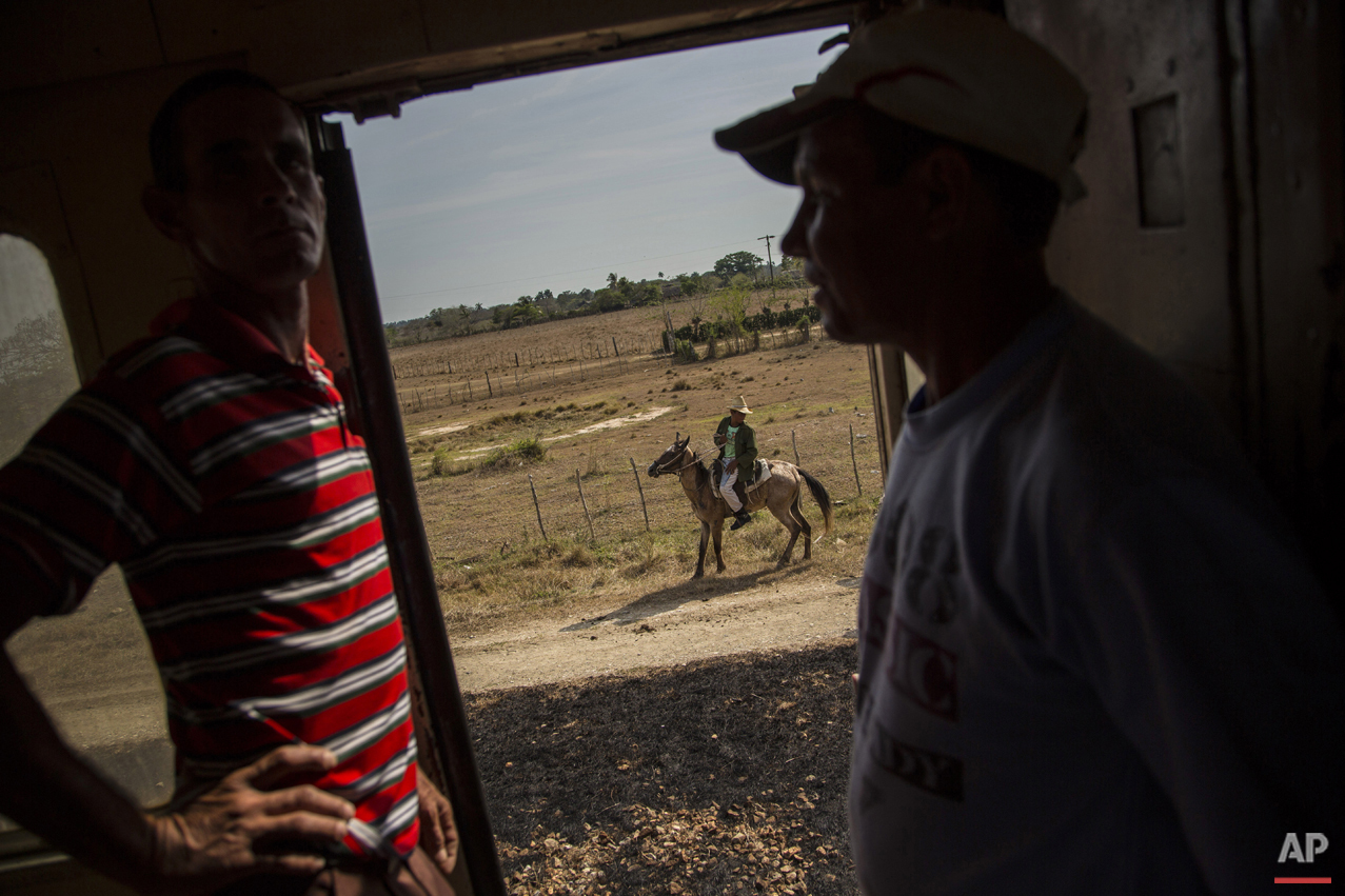  In this March 23, 2015 photo, passengers pass the time chatting on the landing of a train car as a farmer rides his horse alongside the tracks in the province of Holguin in Cuba. Cuba became the first Latin American country with a train system in th