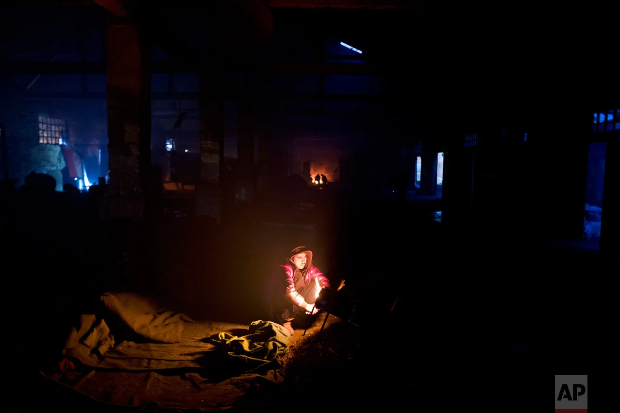 In this Sunday, Feb. 12, 2017 photo, unaccompanied minor Mohammed, 16, a migrant from Jalalabad, Afghanistan, sits around a fire to shield from the evening cold in an abandoned warehouse where he and other migrants took refuge in Belgrade, Serbia. (AP Photo/Muhammed Muheisen)