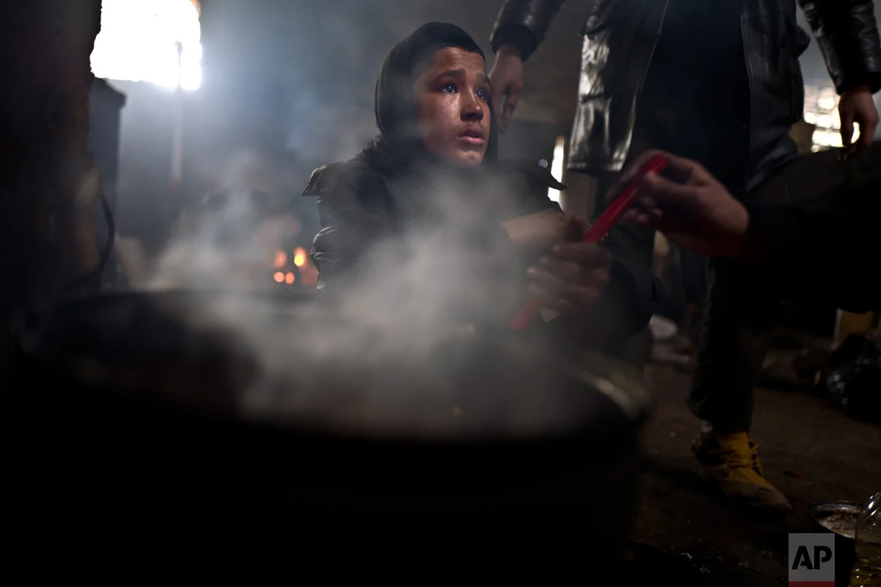 In this Saturday, Feb. 4, 2017 photo, unaccompanied minor Liaqat, 12, a migrant from Khogyani, Afghanistan, cooks on a fire in an abandoned warehouse where he and other migrants took refuge in Belgrade, Serbia. (AP Photo/Muhammed Muheisen)