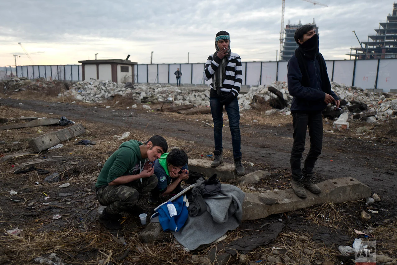 In this Thursday, Feb. 2, 2017 photo, unaccompanied minors, Shams, 13, a migrant from Laghman, Afghanistan, center wearing a black and white shirt and Amir, 14, a migrant from Peshawar, Pakistan, stand next to other migrants shaving using a hand-mirror outside an abandoned warehouse where they took refuge in Belgrade, Serbia. (AP Photo/Muhammed Muheisen)