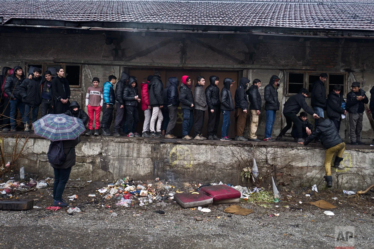 In this Saturday, Feb. 4, 2017 photo, unaccompanied minor, Ali, 12, a migrant from Jalalabad, Afghanistan, left wearing a red pants, queue for food outside an abandoned warehouse where he and other migrants took refuge in Belgrade, Serbia. (AP Photo/Muhammed Muheisen)