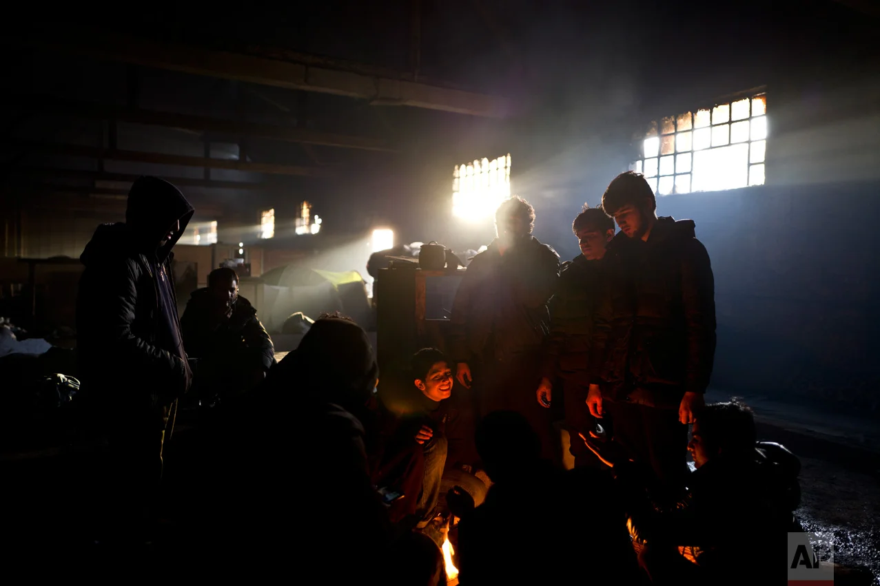 In this Sunday, Feb. 5, 2017 photo, unaccompanied minor Rasool, 12, center, a migrant from Jalalabad, Afghanistan, laughs while sitting with older migrants around a fire in an abandoned warehouse where they took refuge in Belgrade, Serbia. (AP Photo/Muhammed Muheisen)