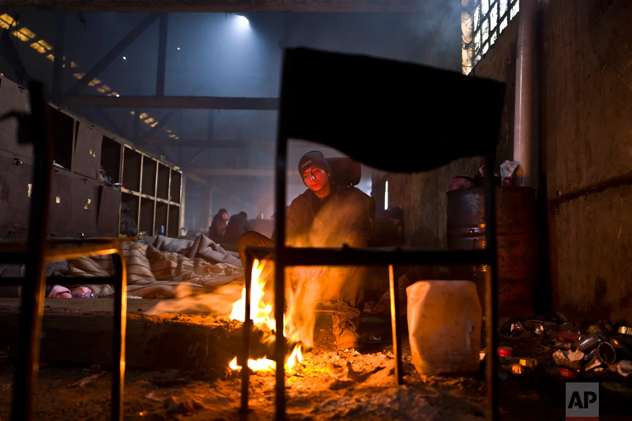 In this Friday, Feb. 3, 2017 photo, unaccompanied minor Amir, 14, a migrant from Peshawar, Pakistan, sits around a fire to warm himself from the morning cold in an abandoned warehouse where he and other migrants took refuge in Belgrade, Serbia. (AP Photo/Muhammed Muheisen)