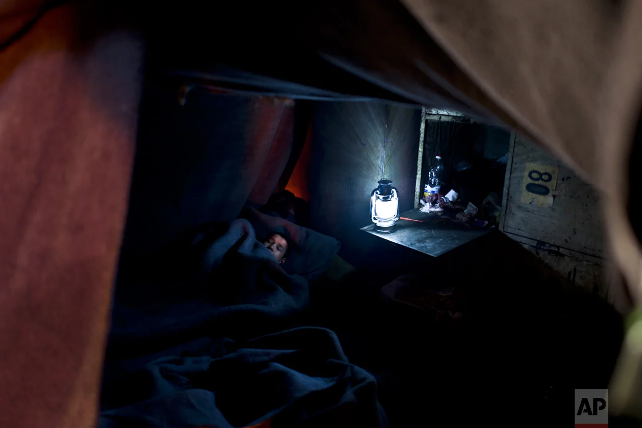 In this Wednesday, Feb. 15, 2017 photo, unaccompanied minor Liaqat, 12, a migrant from Khogyani, Afghanistan, sleeps on the ground inside a makeshift room made of blankets in an abandoned warehouse where he and other migrants took refuge in Belgrade, Serbia. (AP Photo/Muhammed Muheisen)