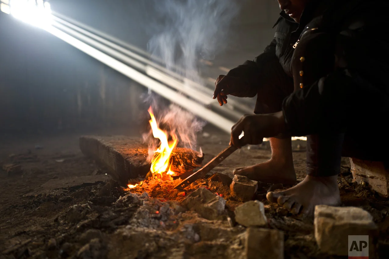 In this Monday, Jan. 30, 2017 photo, unaccompanied minor Obaidullah, 14, a migrant from Wardak, Afghanistan, warms his legs and hands around a fire in an abandoned warehouse where he and other migrants took refuge in Belgrade, Serbia. (AP Photo/Muhammed Muheisen)