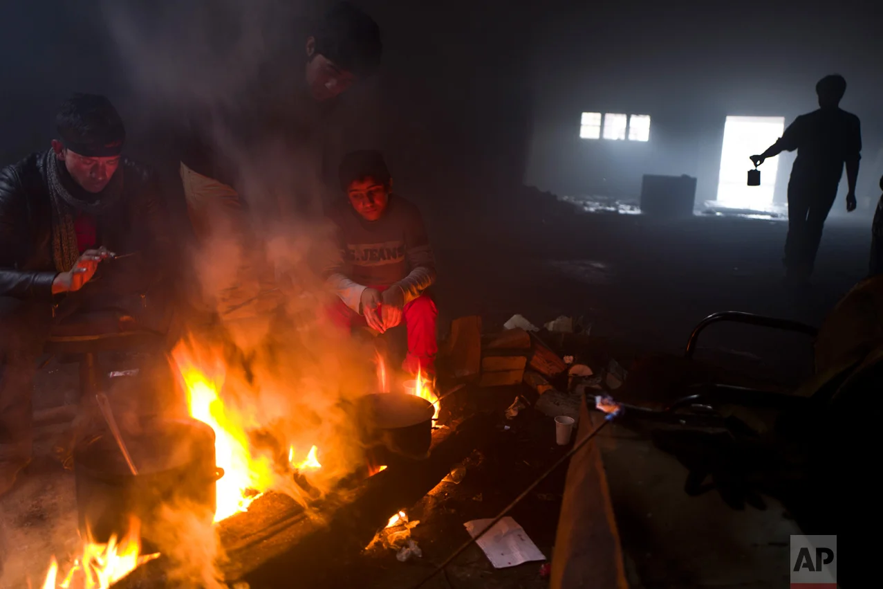 In this Saturday, Feb. 4, 2017 photo, unaccompanied minor, Ali, 12, a migrant from Jalalabad, Afghanistan, sits while cooking on a fire in an abandoned warehouse where he and other migrants took refuge in Belgrade, Serbia. (AP Photo/Muhammed Muheisen)