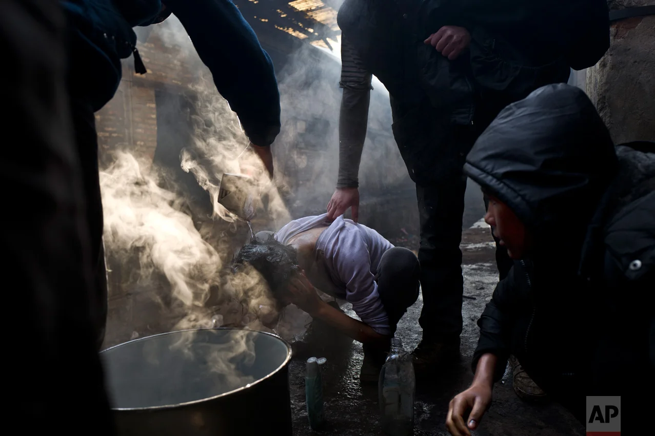 In this Monday, Jan. 30, 2017 photo, unaccompanied minor Amir, 14, a migrant from Peshawar, Pakistan is helped by other migrants to wash his hair while his friend Liaqat, 12, right waits his turn, in an abandoned warehouse where they took refuge in Belgrade, Serbia. (AP Photo/Muhammed Muheisen)