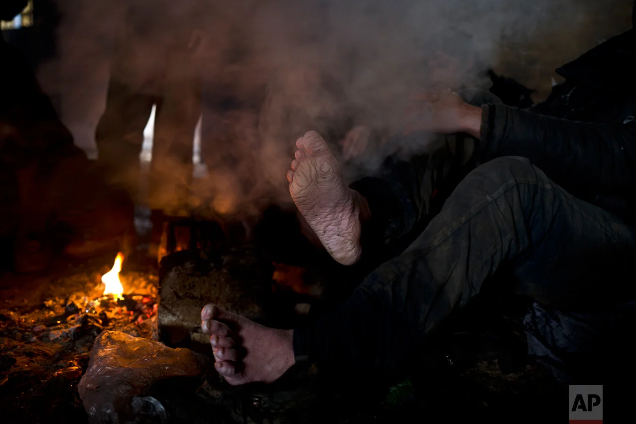 In this Wednesday, Feb. 8, 2017 photo, unaccompanied minor Matiuallah, 14, a hearing impaired and unable to speak migrant from Afghanistan, warms his feet by a fire shortly after arriving from the Bulgarian border to an abandoned warehouse in Belgrade, Serbia. (AP Photo/Muhammed Muheisen)