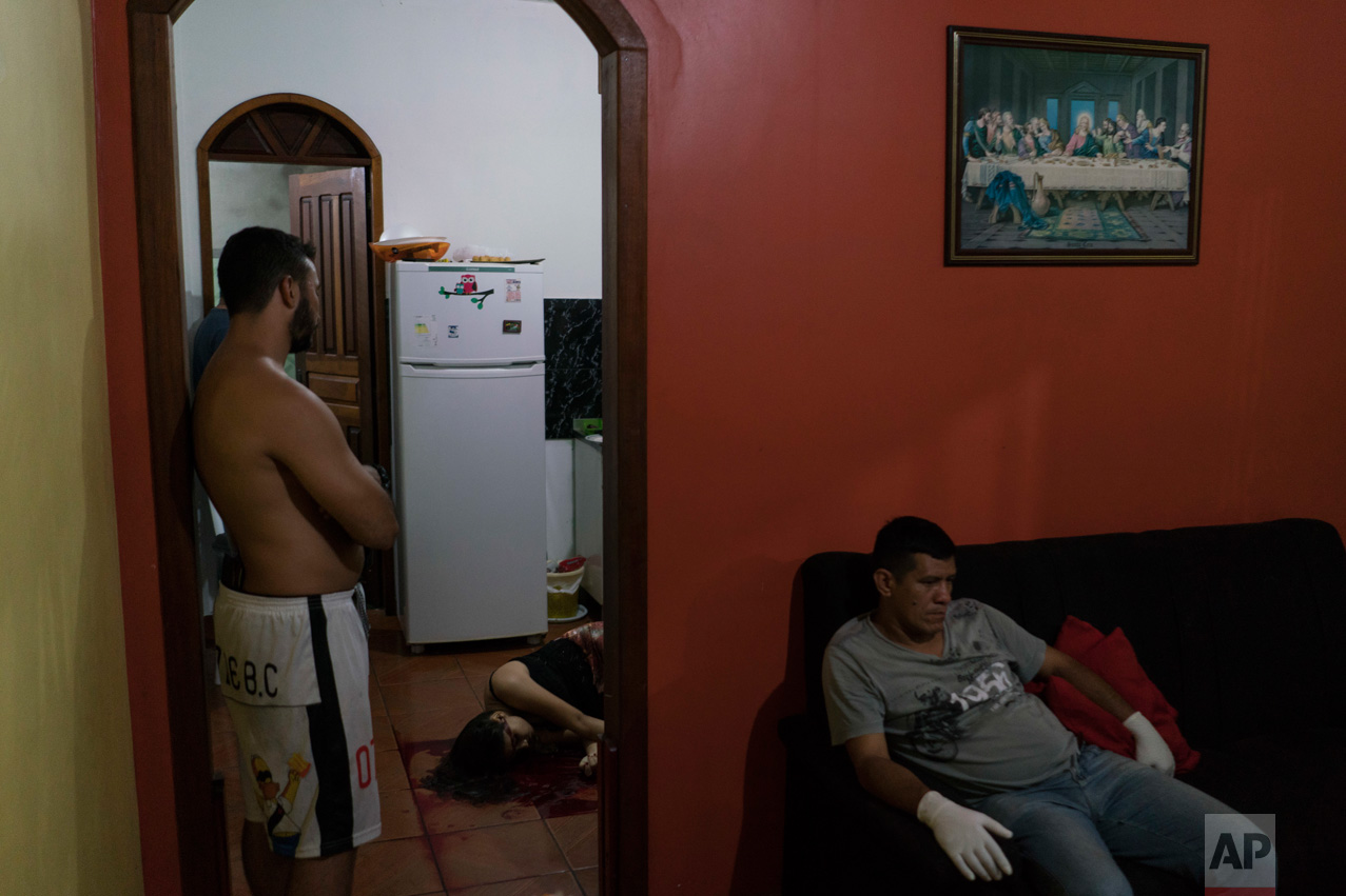 In this Feb. 5, 2017 photo, a gloved morgue worker rests at a home where the body of a woman lies on the kitchen floor after she was shot to death under unclear circumstances in Manaus, Brazil. The increasingly violent city is a thoroughfare for drug trafficking across South America, where authorities suspect most murders are gang related. (AP Photo/Felipe Dana)