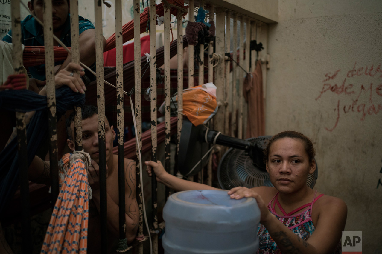 In this Feb. 6, 2017 photo, female detainee Regiane stands locked in a corridor between two holding cells overcrowded with men at a police station near Manaus, Brazil. The station had two cells where 24 people were being housed despite an official capacity of for eight. (AP Photo/Felipe Dana)