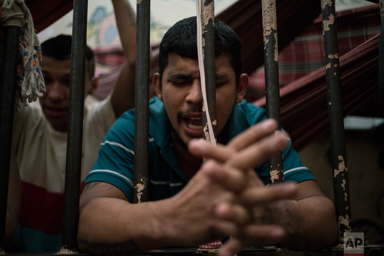 In this Feb. 6, 2017 photo, a detainee prays inside an overcrowded cell at a police station near Manaus, Brazil. All 24 detainees being held in this space made for eight said they hoped to avoid being transferred to a bigger prison under gang rule. (AP Photo/Felipe Dana)