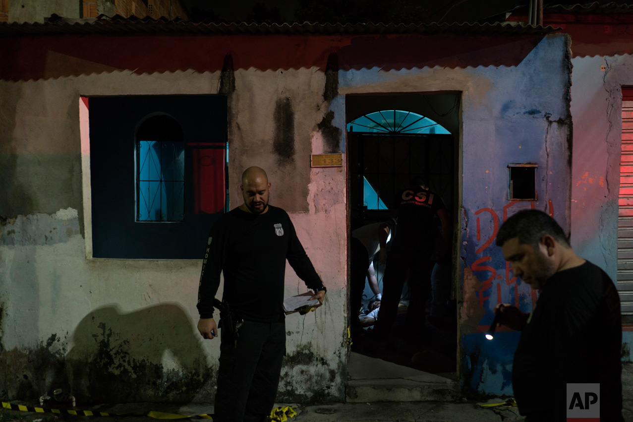 In this Feb. 5, 2017 photo, police inspect a home where a murder victim lies on the floor in Manaus, Brazil. The increasingly violent city is a thoroughfare for drug trafficking across South America, where authorities suspect most murders are gang related. (AP Photo/Felipe Dana)
