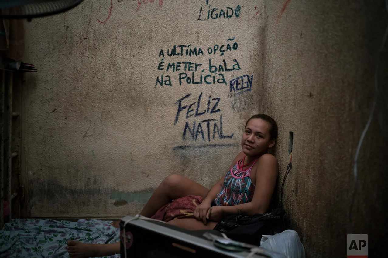 In this Feb. 6, 2017 photo, female prisoner Regiane sits on her bed inside a corridor between two cells crowded with men at a police station near Manaus, Brazil. The message on the wall reads in Portuguese: "The last option is to put a bullet in the police. Merry Christmas." (AP Photo/Felipe Dana)