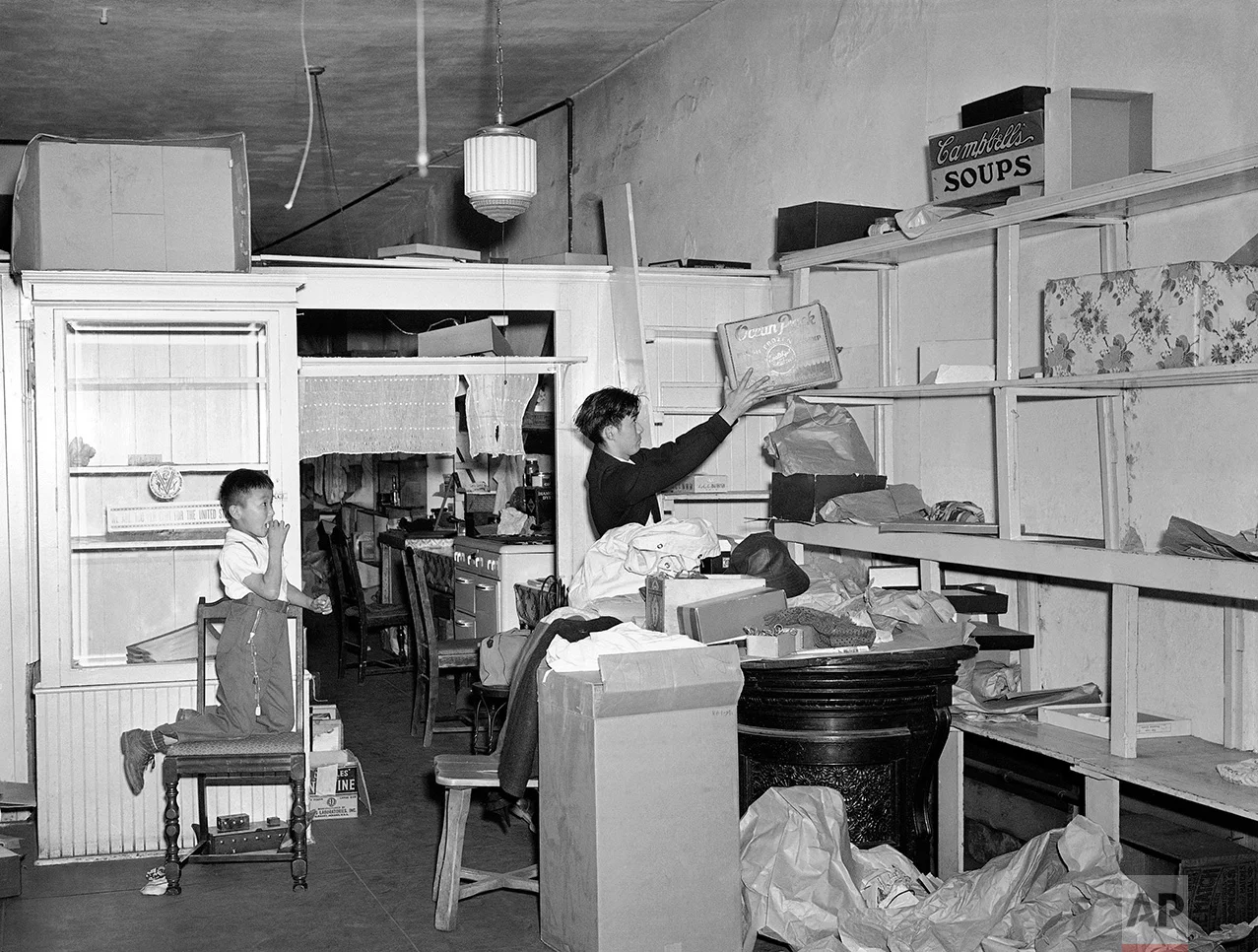 In preparation for the evacuation of Los Angeles' famed "Little Tokyo" section as a result of the ordering of 300,000 aliens and American-born Japanese from various Pacific coast combat zones, 20-year-old Yeichi Shoji, right, helps clear the shelves of the dry goods store operated by his parents, March 5, 1942, as Taro Sasai, 7, looks on. Shoji was born in the living quarters at the rear of the store, his elder brother is a soldier in the U.S. Army. (AP Photo/John T. Burns)