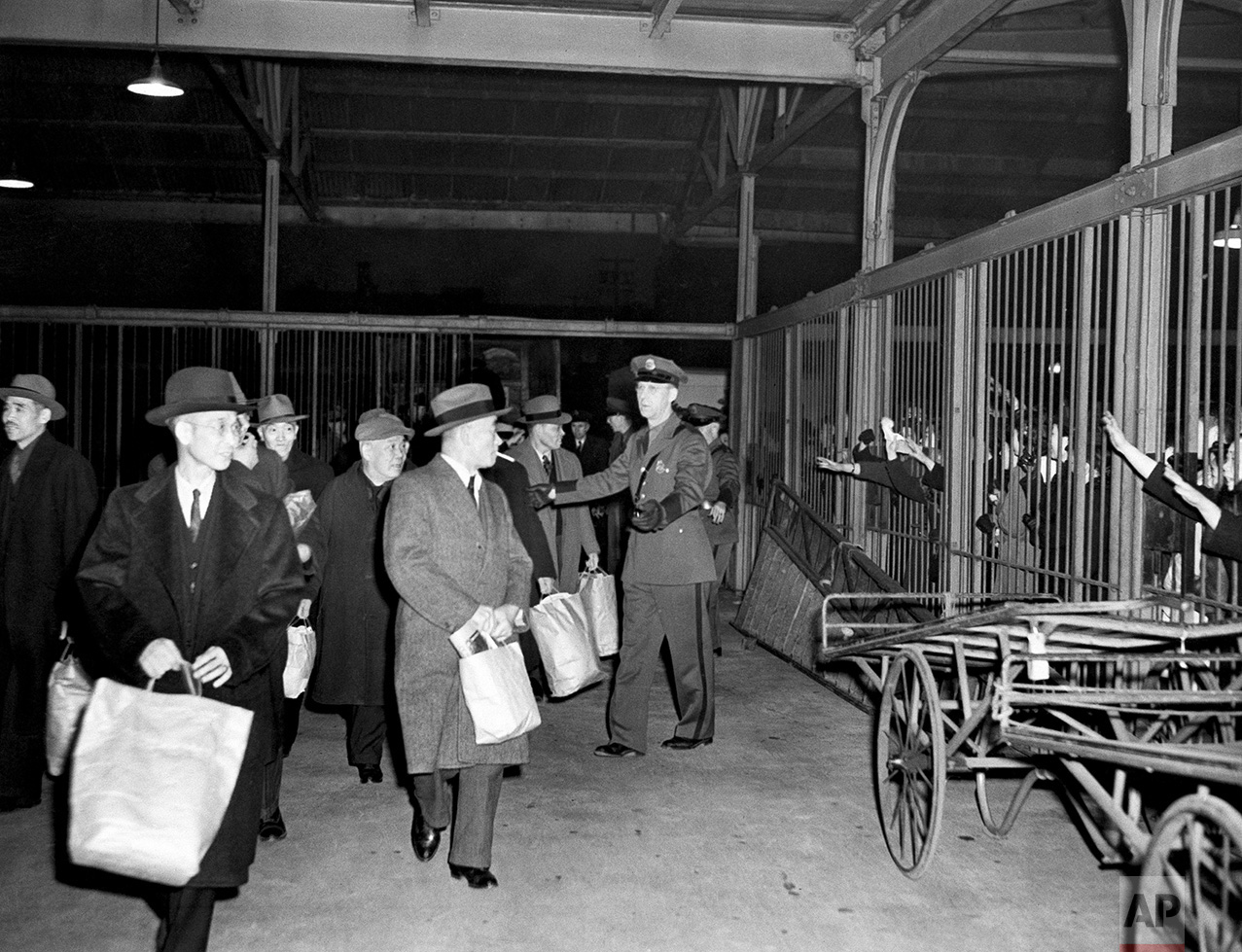 Interned Japanese, carrying belongings in paper bags, leave Seattle by train for Fort Missoula, Montana, March 19, 1942, while relatives waved through station cars, right. A group of 150 internees had been held in the Seattle immigration station. (AP Photo)