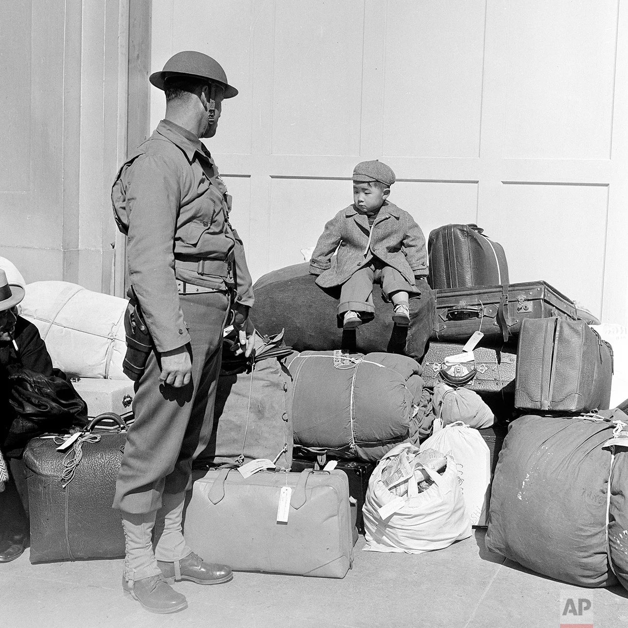 In this April 6, 1942 photo, a boy sits on a pile of baggage as he waits for his parents, as a military policeman watches in San Francisco. More than 650 citizens of Japanese ancestry were evacuated from their homes and sent to Santa Anita racetrack, an assembly center for war relocation of alien and American-born Japanese civilians. (AP Photo)