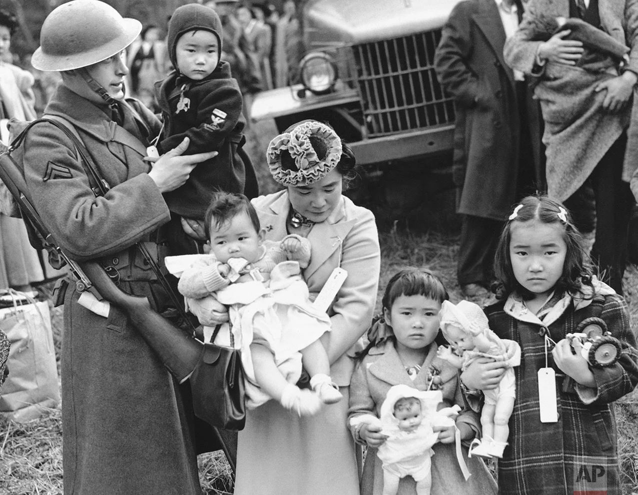 In this March 30, 1942 photo, Cpl. George Bushy, left, a member of the military guard which supervised the departure of 237 Japanese people for California, holds the youngest child of Shigeho Kitamoto, center, as she and her children are evacuated from Bainbridge Island, Wash. Roughly 120,000 Japanese immigrants and Japanese-Americans were sent to desolate camps that dotted the West because the government claimed they might plot against the U.S. (AP Photo)