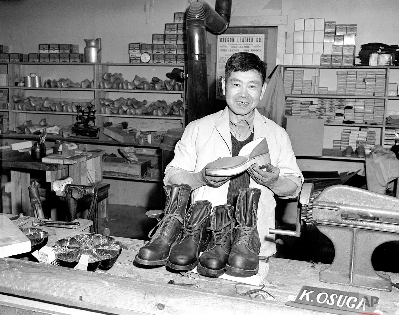 Mitsutaro Miyahara is in charge of the shoe shop at Tule Lake, Calif., Japanese relocation center. Miyahara holds a pair of shoes he made of wood and he made the leather ones in the foreground, May 21, 1943. (AP Photo)