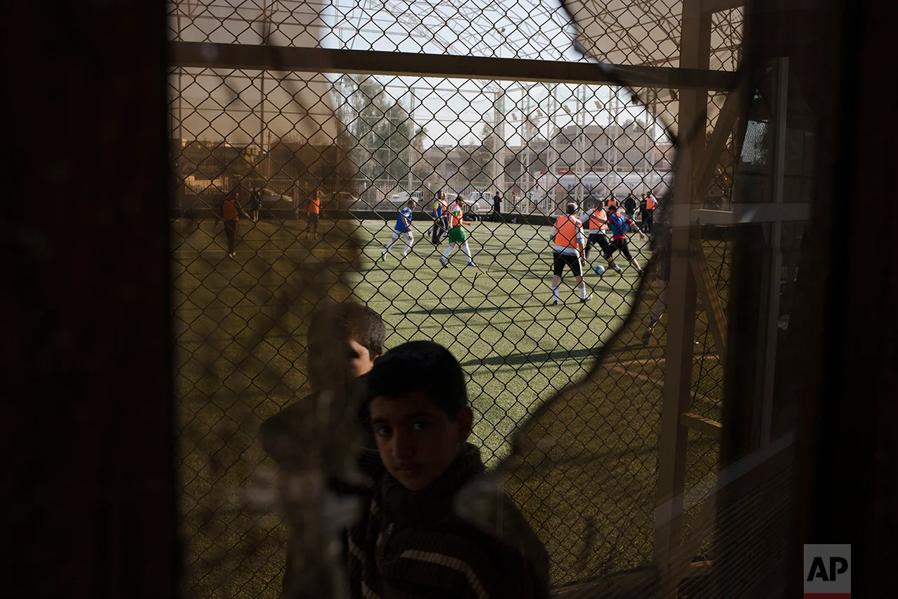  A child passes a broken window, damaged by fighting between Iraqi forces and Islamic State militants, while Mosul residents play soccer in the background on Feb. 7, 2017. After months of fighting, Mosul residents can finally practice their favorite 