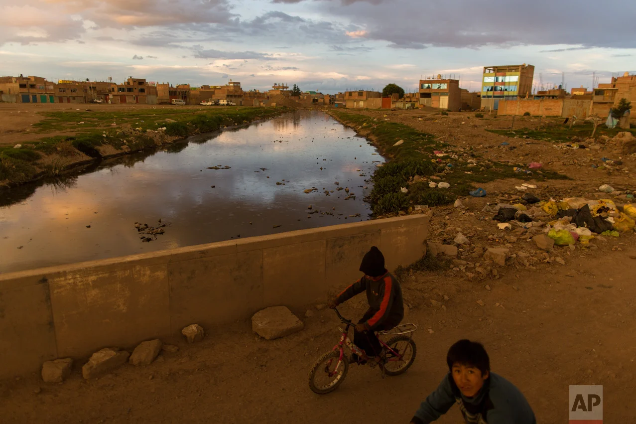 In this Feb. 1, 2017 photo, children ride bikes along the Torococha River near a municipal waste treatment plant with water that flows into Lake Titicaca, in Juliaca, in the Puno region of Peru. Many of the more than 400,000 tourists who visit Lake Titicaca from Peru each year stop first in Juliaca, a town that produces 200 tons of trash daily, much of it winding up in a river that has turned into a conveyor belt of waste heading into the lake. (AP Photo/Rodrigo Abd)