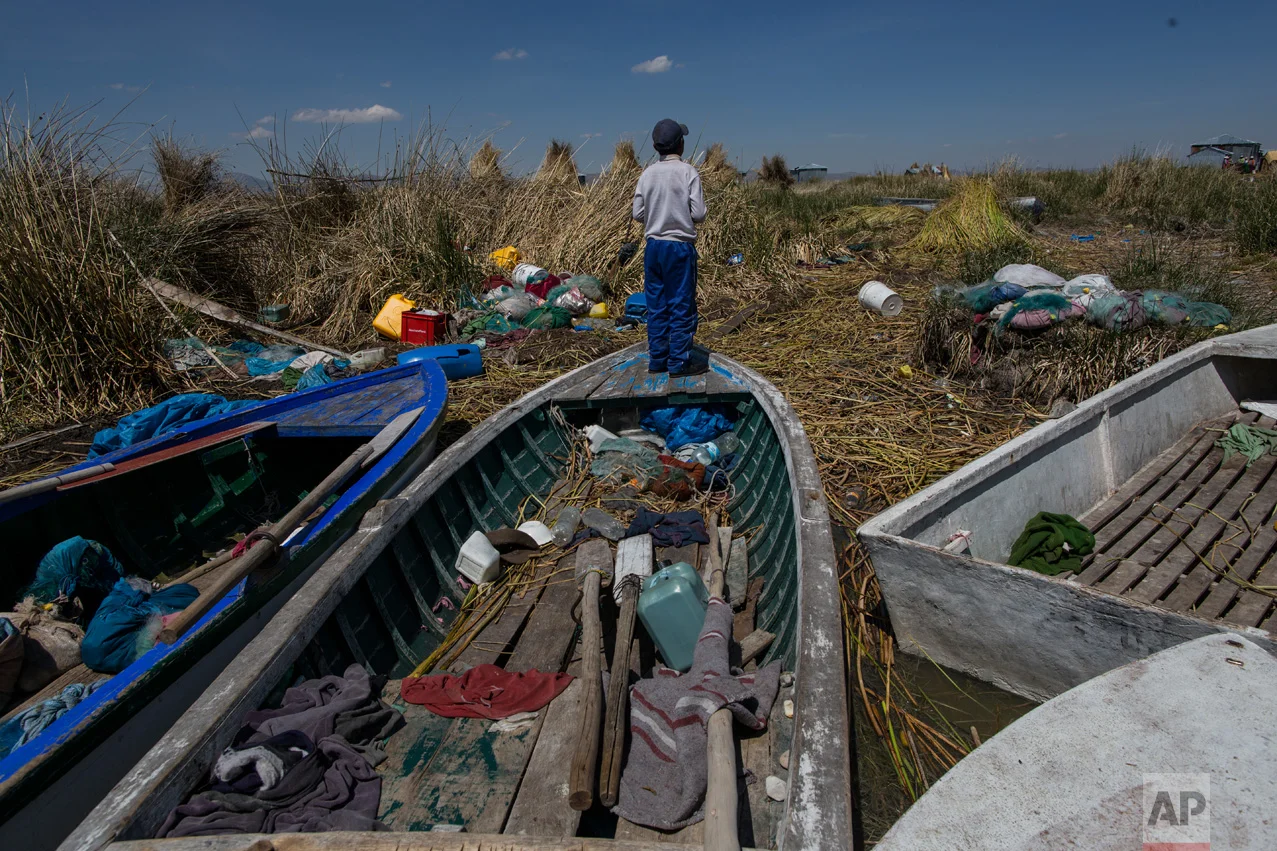 In this Feb. 2, 2017 photo, a boy stands on a fishing boat on the littered shore of Lake Titicaca in Kapi Cruz Grande, in the Puno region of Peru. The camouflage-colored Titicaca water frogs that used to be in abundance have thinned in numbers and have been placed on a “critically endangered” list by the International Union for Conservation of Nature and just 10,000 remain. (AP Photo/Rodrigo Abd)