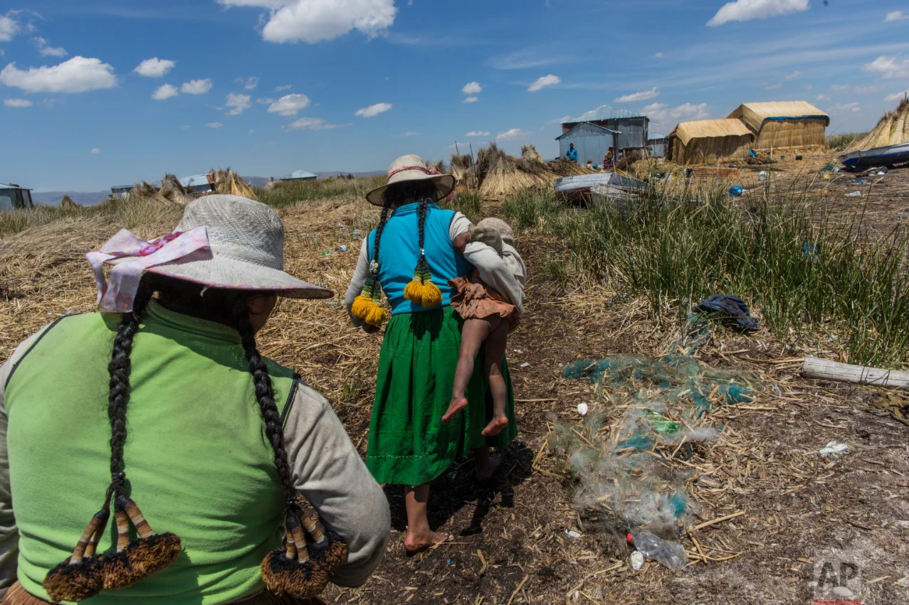 In this Feb. 2, 2017 photo, a woman carries her baby home in Kapi Cruz Grande, a village on the trash filled shores of Lake Titicaca in the Puno region of Peru. Peru’s new president, Pedro Pablo Kuczynski, a former Wall Street banker who lived just 40 kilometers (25 miles) from the lake as a youth, has made access to clean water one of the priorities of his presidency. (AP Photo/Rodrigo Abd)