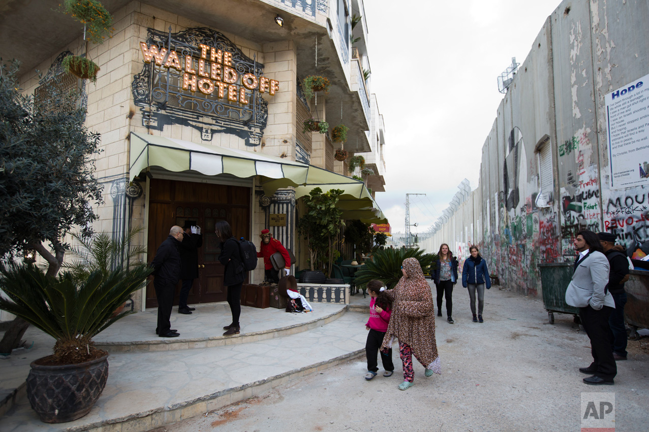  People pass by the "The Walled Off Hotel" and the Israeli security barrier in the West Bank city of Bethlehem, Friday, March 3, 2017. The owner of a guest house packed with the elusive artist Banksy's work has opened the doors of his West Bank estab