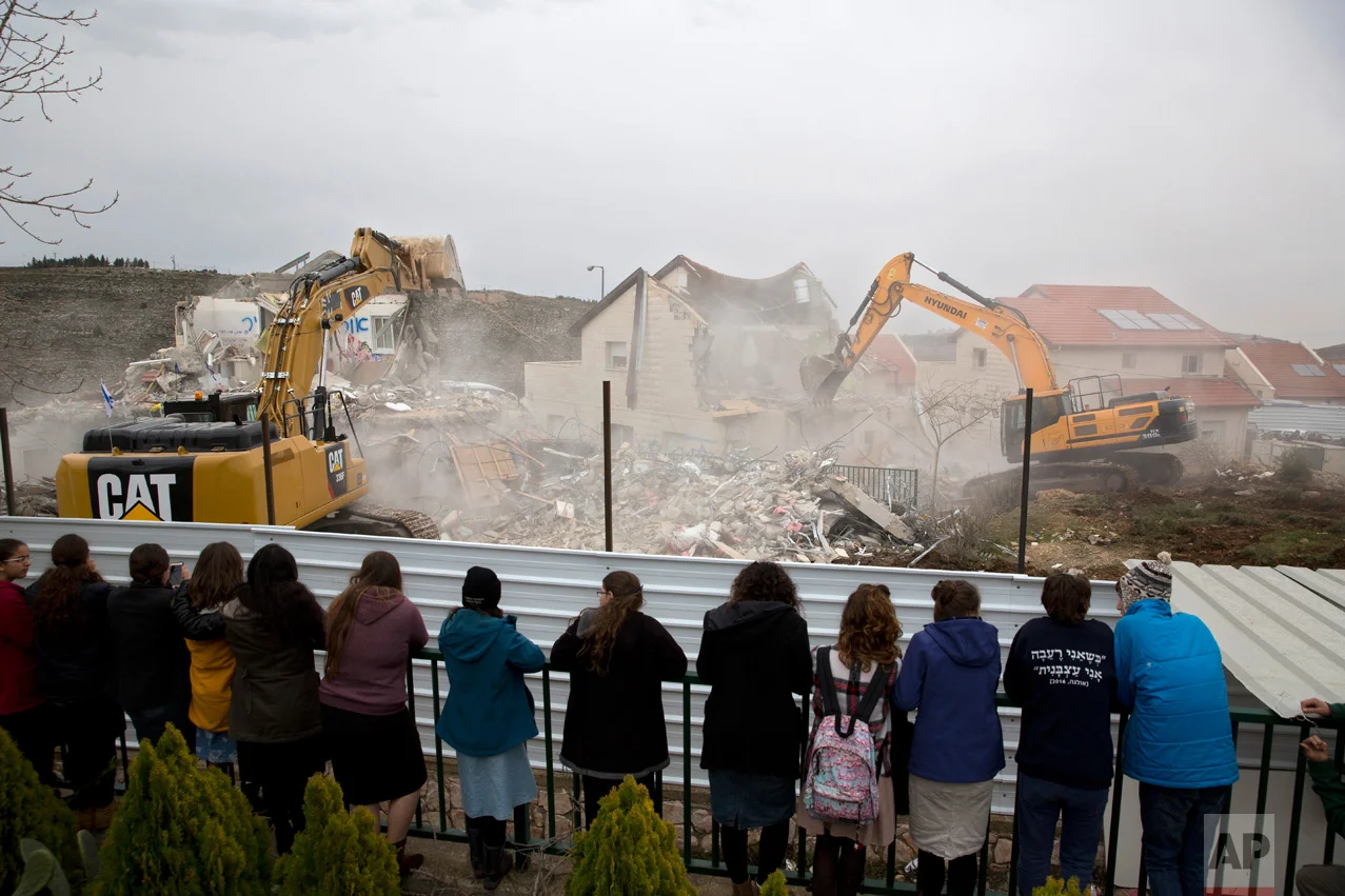 Israeli settlers watch as bulldozers demolish houses in the West Bank settlement of Ofra, Wednesday, March 1, 2017. Israeli forces are demolishing nine homes in the heart of the West Bank settlement after the Supreme Court ruled they were built on private Palestinian land. (AP Photo/Sebastian Scheiner)