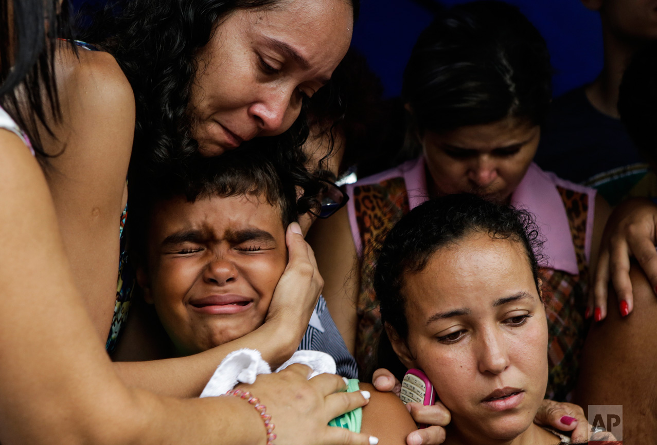 Kailua, center, son of slain civil police officer Mario Marcelo de Albuquerque Espirito, is comforted during his father's funeral, alongside his mother Patricia Albuquerque, right, in Serra, Espirito Santo state, Brazil, Wednesday, Feb 8, 2017. Mario Marcelo de Albuquerque was shot to death when he tried to impede a robbery. (AP Photo/Diego Herculano)