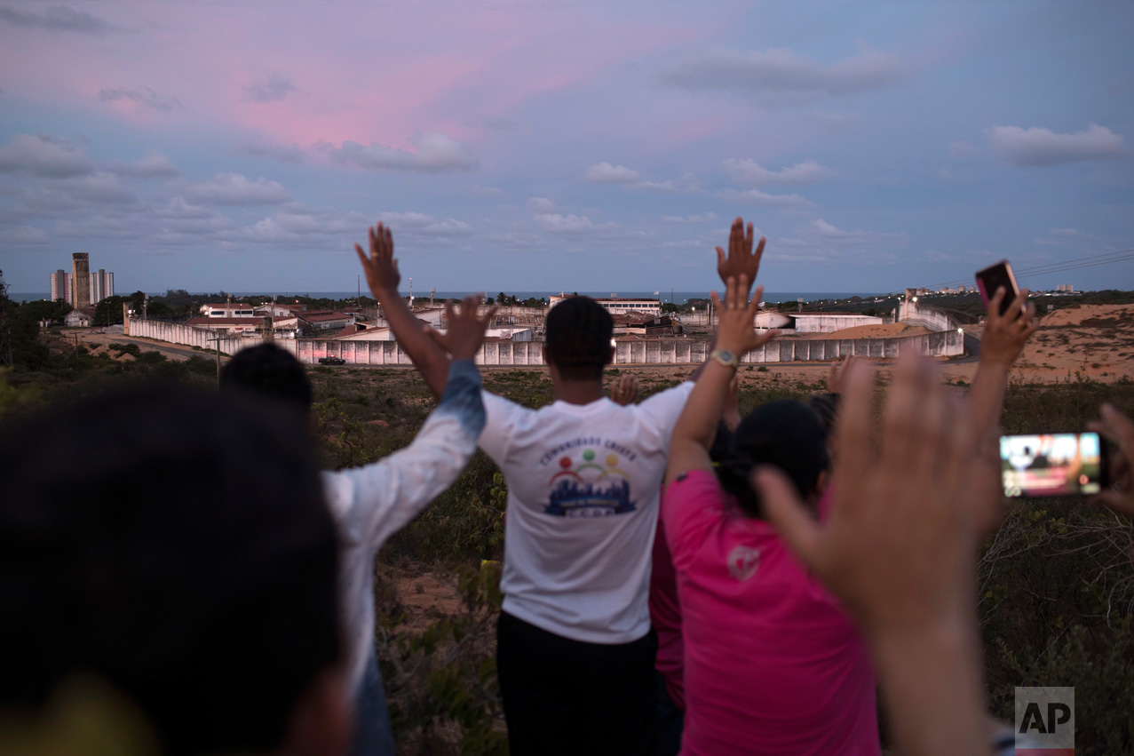 In this Jan. 20, 2017 photo, people pray for peace as they face Alcacuz prison in Nisia Floresta, near Natal, Brazil. Authorities acknowledge that Alcacuz is beyond saving. Rio Grande do Norte state Gov. Robinson Faria has announced it will close, though only after three new prisons are ready. In the meantime, an emergency force of corrections agents has been sent in to establish order and repair the damaged facility. (AP Photo/Felipe Dana)