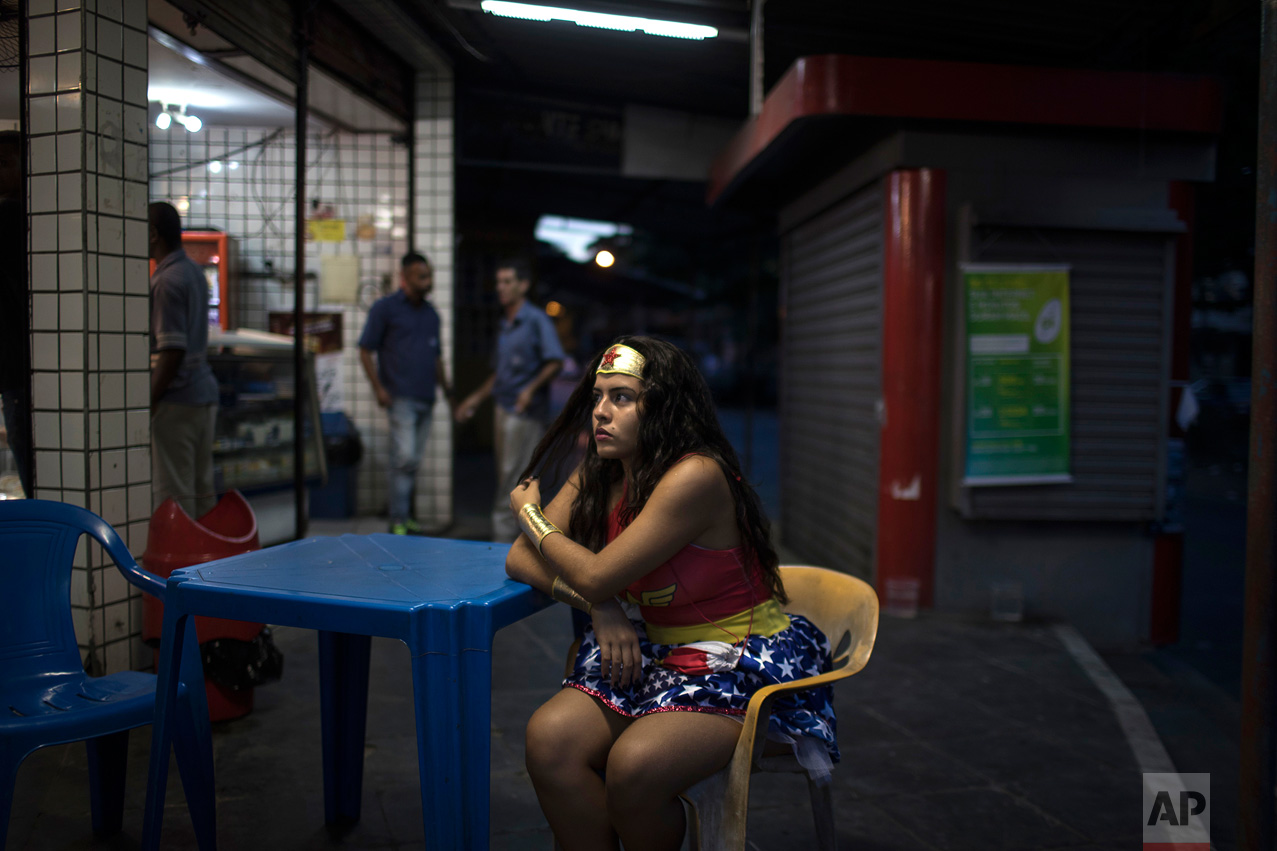 A reveler wearing a wonder woman costume sits at a bar during carnival festivities at the Cidade de Deus, or "City of God" slum in Rio de Janeiro, Brazil, Monday, Feb. 27, 2017. (AP Photo/Felipe Dana)