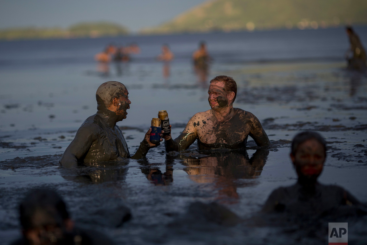 Two men toast beer while wading in mud during the traditional "Bloco da Lama" or "Mud Street" carnival party, in Paraty, Brazil, Saturday, Feb. 25, 2017. Legend has it the "bloco" was born in 1986 after local teens hiking in a nearby mangrove forest smeared themselves with mud to discourage mosquitoes and then wandered through Paraty. The party grew year after year, but revelers eventually were banned from parading in the colonial downtown after shopkeepers complained pristine white walls were stained with the hard-to-remove mud. (AP Photo/Mauro Pimentel)