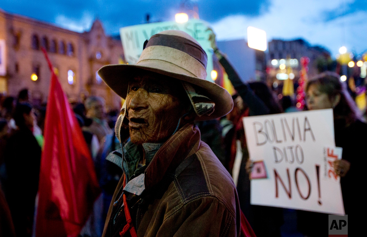 A Quechua Indian watches a protest march against Bolivia's President Evo Morales, while a woman holds a sign with a message that reads in Spanish; "Bolivia said no!" regarding a referendum ruling out his run for a fourth term, in La Paz, Bolivia, Tuesday, Feb. 21, 2017. (AP Photo/Juan Karita)