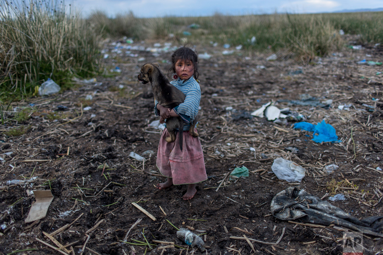  In this Feb. 4, 2017 photo, Melinda Quispe walks on the trash strewn shore of Lake Titicaca, as she holds her dog, in her village Kapi Cruz Grande, in the Puno region of Peru. The governments of Peru and Bolivia signed a pact in January to spend mor