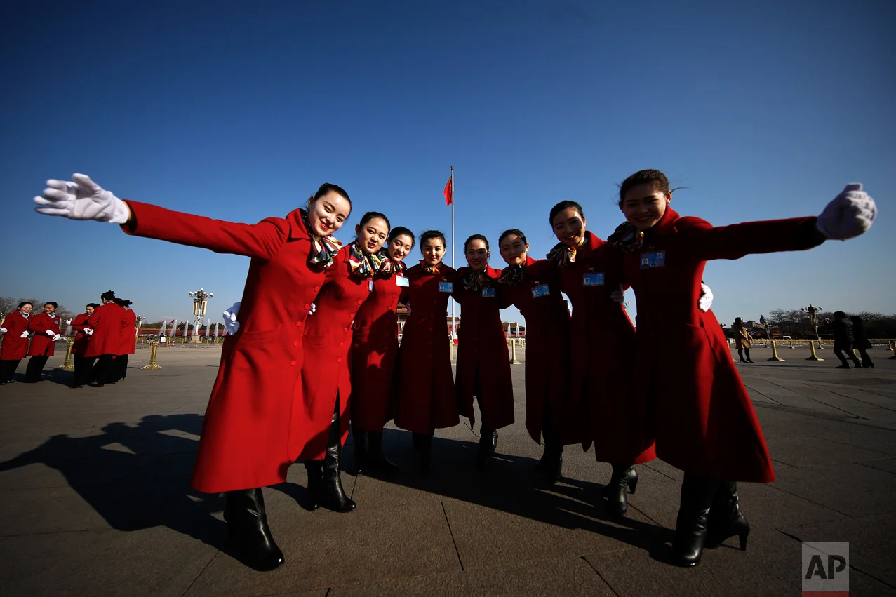 In this Sunday, March 5, 2017 photo, hospitality staff pose for photographs on Tiananmen Square during the National People's Congress held at the Great Hall of the People in Beijing. (AP Photo/Andy Wong)