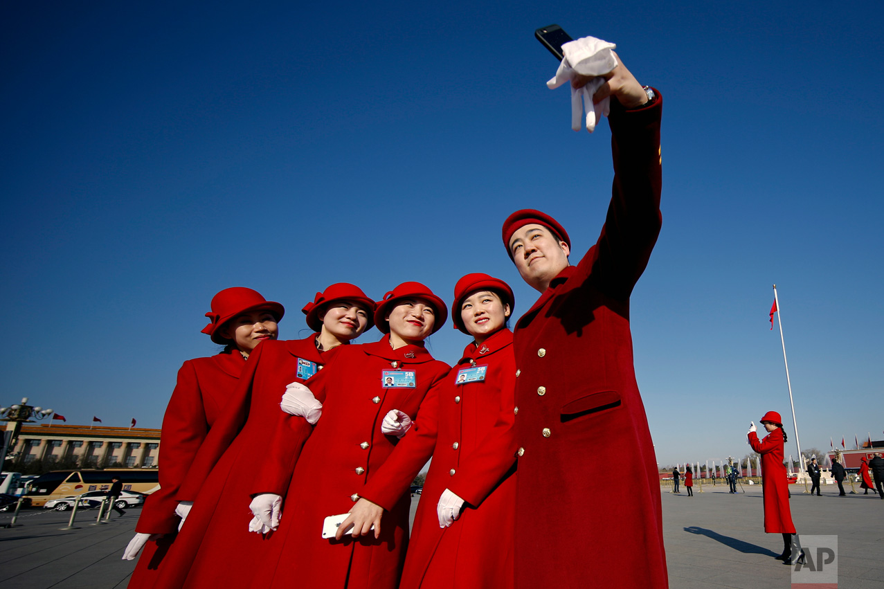 In this Sunday, March 5, 2017 photo, hospitality staff take selfies on Tiananmen Square during the National People's Congress held at the Great Hall of the People in Beijing. (AP Photo/Andy Wong)