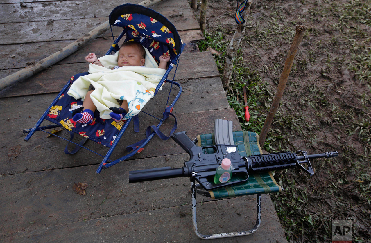 In this Tuesday, Feb. 28, 2017 photo, 3-month-old Junior Alexis Patino, son of FARC rebel Deisy Garcia, sleeps next to his mother's weapon at a rebel camp in a demobilization zone in La Carmelita, in Colombia's southwestern Putumayo state. Amid the makeshift tents and communal kitchens where Colombia's largest rebel army is preparing to lay down its weapons, a new sound is emerging: the cries of babies. (AP Photo/Fernando Vergara)