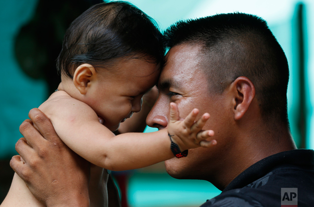 In this Tuesday, Feb. 28, 2017 photo, FARC rebel Vicente Pulecio plays with his 9-month-old son Dainer inside their tent at a rebel camp in a demobilization zone in La Carmelita, in Colombia's southwestern Putumayo state. Pulecio's wife Jerly Suarez gave birth to their son shortly before the FARC began its march to one of the 26 demobilization zones. (AP Photo/Fernando Vergara)