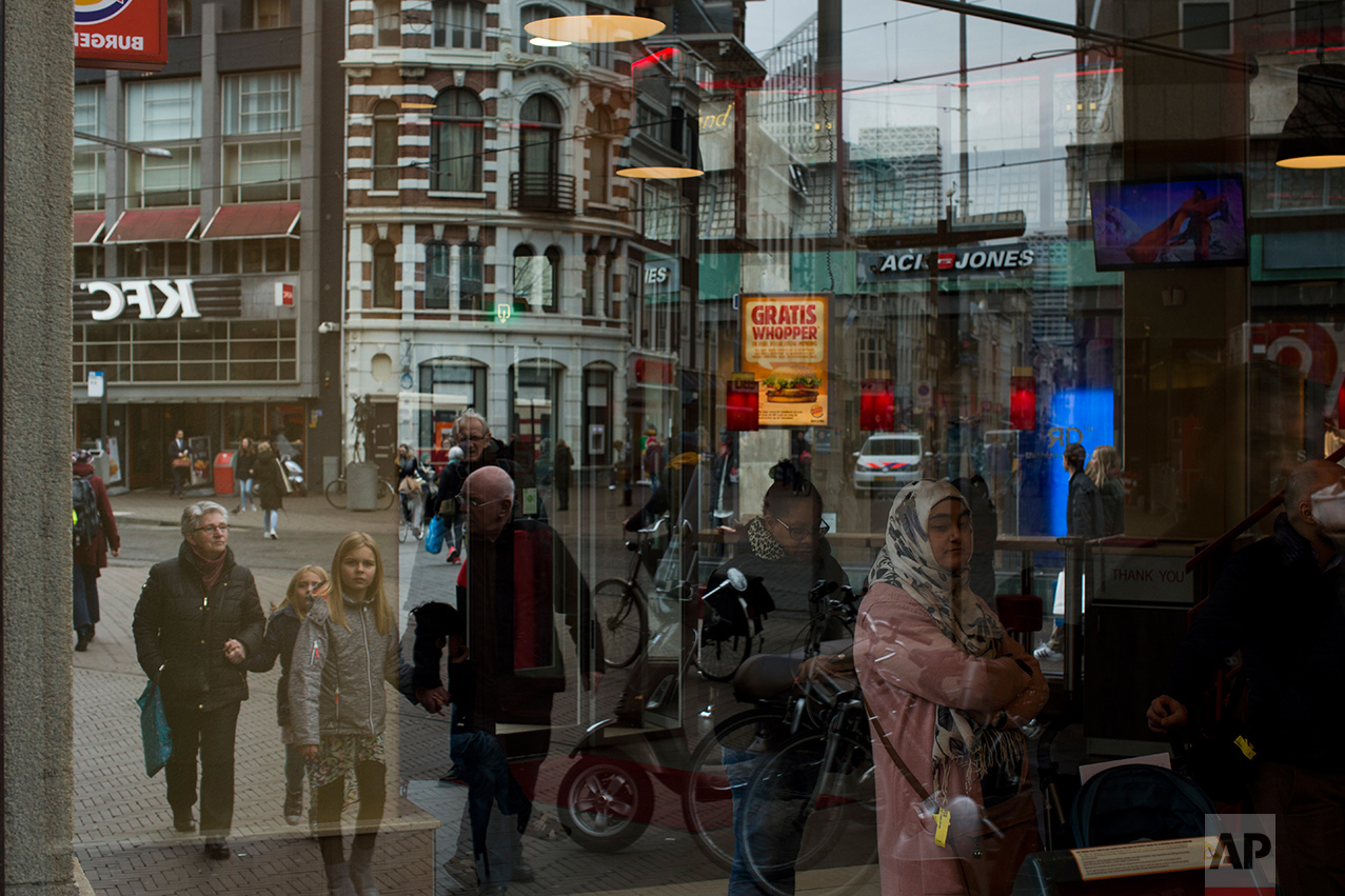 In this Friday, March 3, 2017 photo, people are seen reflected in a restaurant window in The Hague, the Netherlands. Of The Netherlands' 17 million people, just over one in five now have a migrant background _ rising to roughly half-and-half in The Netherlands' four largest melting-pot cities: Amsterdam, Rotterdam, Utrecht and The Hague. (AP Photo/Emilio Morenatti)