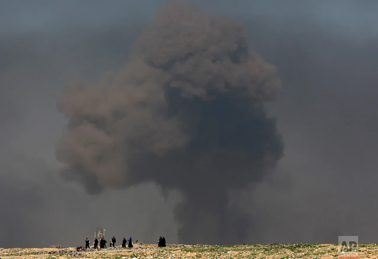 A large plume of smoke rises during fighting between Iraqi security forces and Islamic State militants as civilians walk toward Iraqi security forces after fleeing their homes on the western side of Mosul, Iraq, Thursday, March 9, 2017. (AP Photo/Khalid Mohammed)