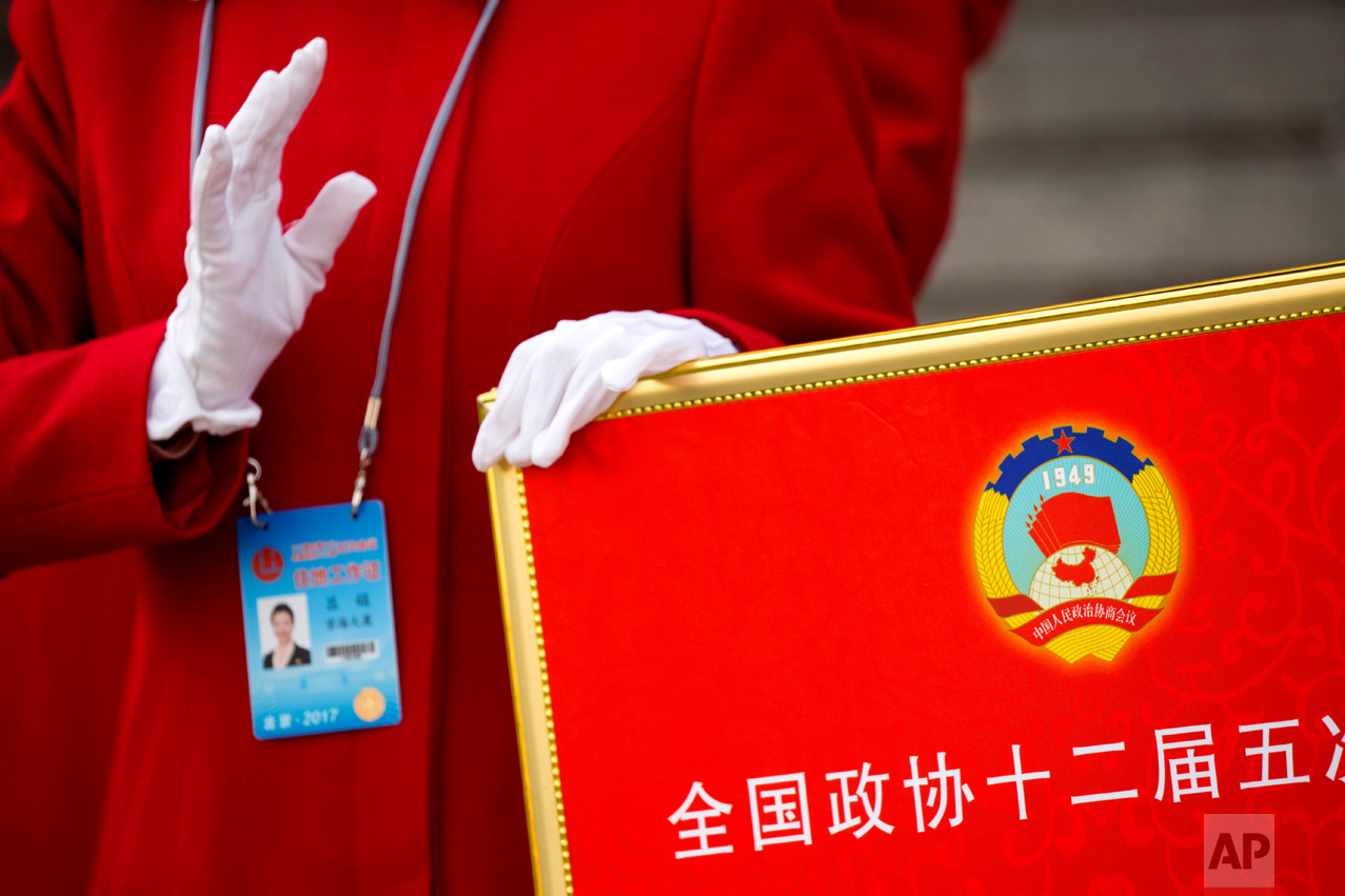 In this Friday, March 3, 2017 photo, a hospitality staff member holds a signboard with the logo of the Chinese People's Political Consultative Congress (CPPCC) as she directs delegates after the end of the opening session of the CPPCC at the Great Hall of the People in Beijing. (AP Photo/Mark Schiefelbein)
