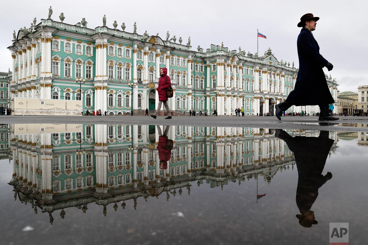 People walk past the Zimny (Winter) Palace at Dvortsovaya Square in St. Petersburg, Russia on Saturday, March 11, 2017. A century after the days that shook the world, the anniversary of the 1917 revolution in Russia is being marked with little official fanfare from the Kremlin. It once was celebrated with pomp and parades but now no longer fits the narrative of political and religious leaders. (AP Photo/Dmitri Lovetsky)