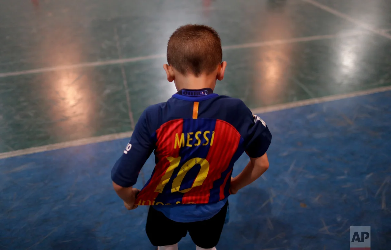 In this Nov. 11, 2016 photo, Benjamin Palandella puts on his Barcelona jersey adorned with Messi's number 10 after a training game at the youth soccer academy Club Social Parque in a working class neighborhood of Buenos Aires, Argentina. After the training game, Benjamin continued to kick the ball even after the other kids had gone home. (AP Photo/Natacha Pisarenko)